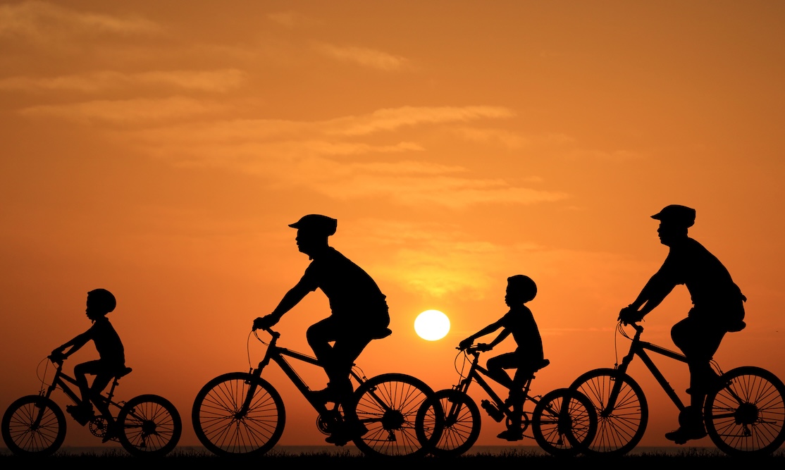 Silhouette family riding bicycle at sunset sky.